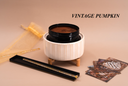 A product display featuring a white ribbed ceramic warmer with a black wickless containing a brown wax melt, set on a beige background with a gold tulle bag, a black tray with a gold-toned accessory, and several cards. The brand name 'VINTAGE PUMPKIN' is printed in black text in the upper right.