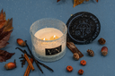 An Autumn Rain Velvet Noble candle on a blue background with decorative fall elements.