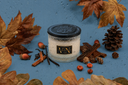 An Autumn Rain Velvet Noble candle on a blue background with decorative fall elements.