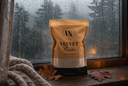 A stand-up pouch of Velvet Powder Carpet powder sits on a wooden windowsill with raindrops on the glass. The pouch is tan and black with a white band near the bottom, and the brand logo.