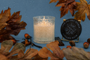 A single wick Autumn Rain candle on a blue background with decorative fall elements.