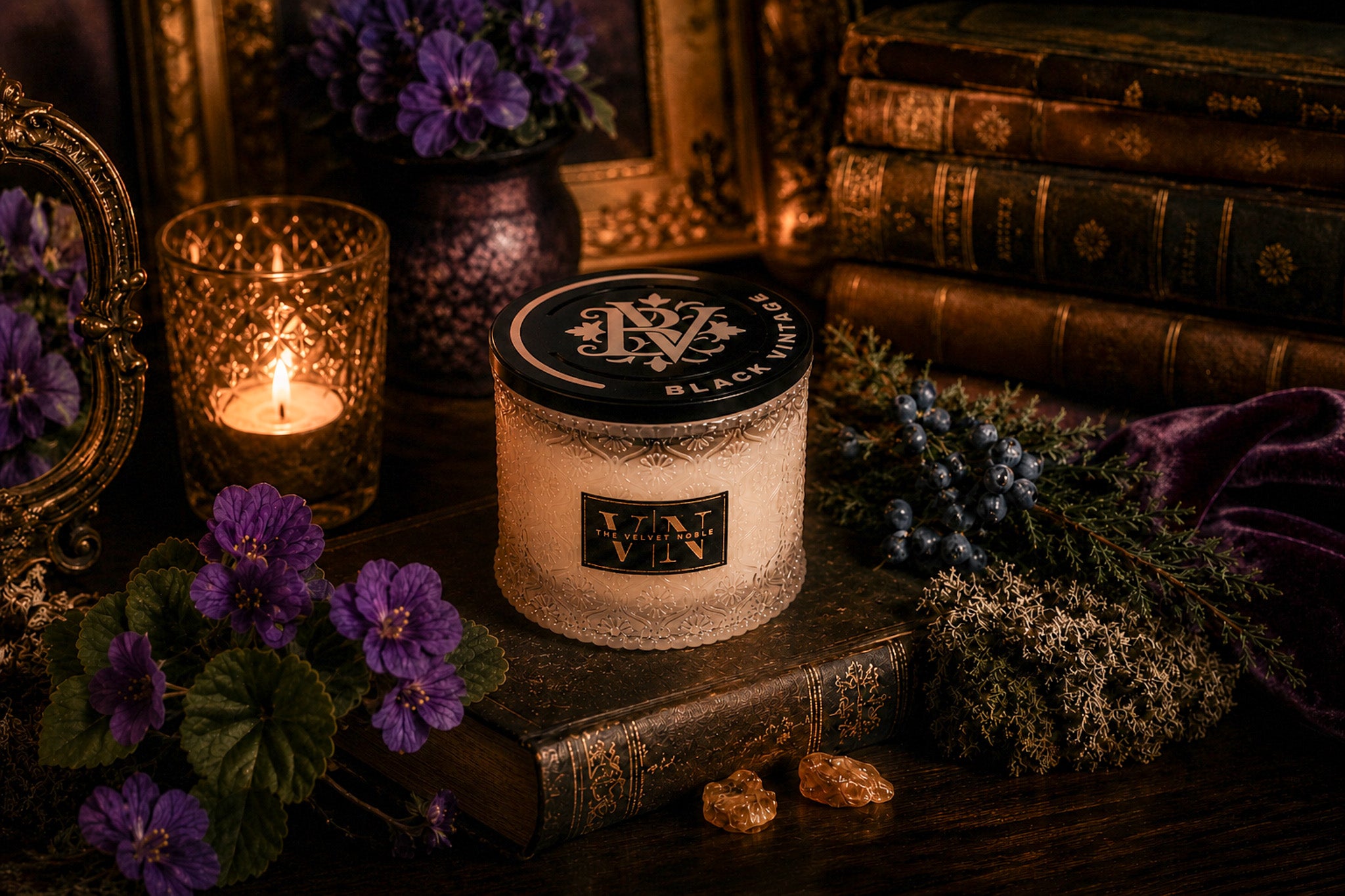 Candle with decorative label on a wooden surface with purple flowers and books in the background