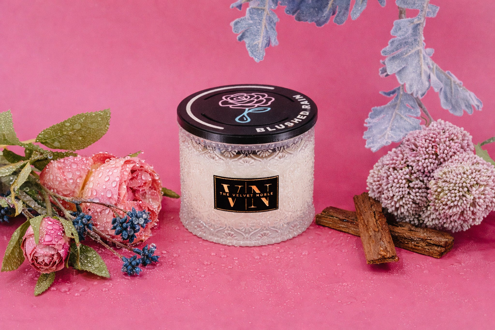 Two Wick Blushed Rain Candle on a pink background with floral elements.
