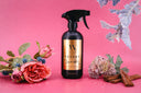 Black spray bottle labeled 'Velvet Sparkle' on a pink background with flowers.