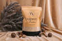 A stand-up pouch of Velvet Powder by The Velvet Noble, styled with cinnamon sticks, pinecones, and evergreen branches on a draped champagne-gold fabric background.