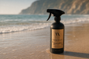 Spray bottle labeled 'Velvet Sparkle' on a beach with ocean and mountains in the background