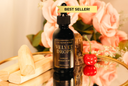 Bottle of 'Velvet Drops' luxury warmer oil with a dropper on a reflective surface with flowers in the background.