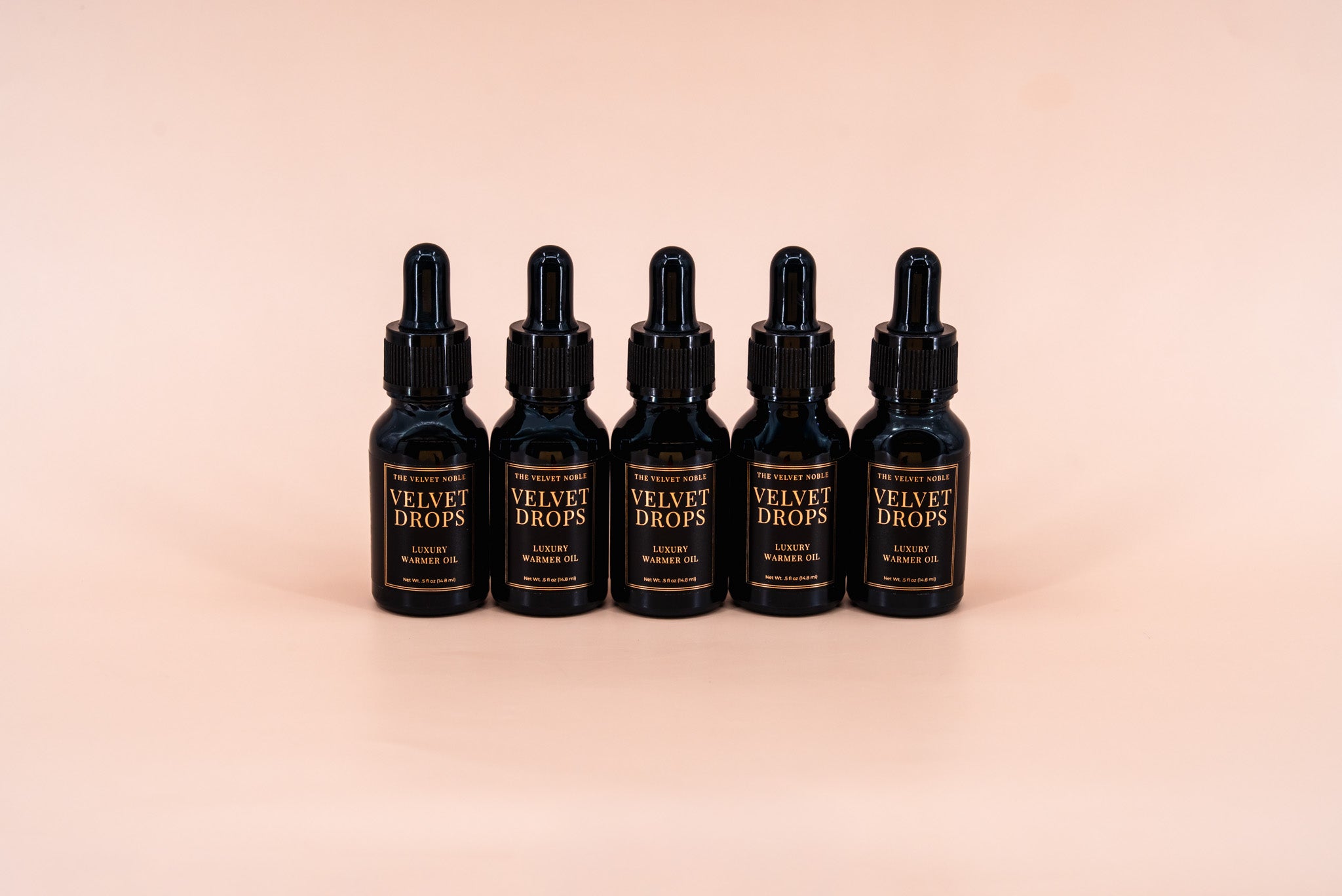 Five black bottles labeled 'Velvet Drops' on a beige background