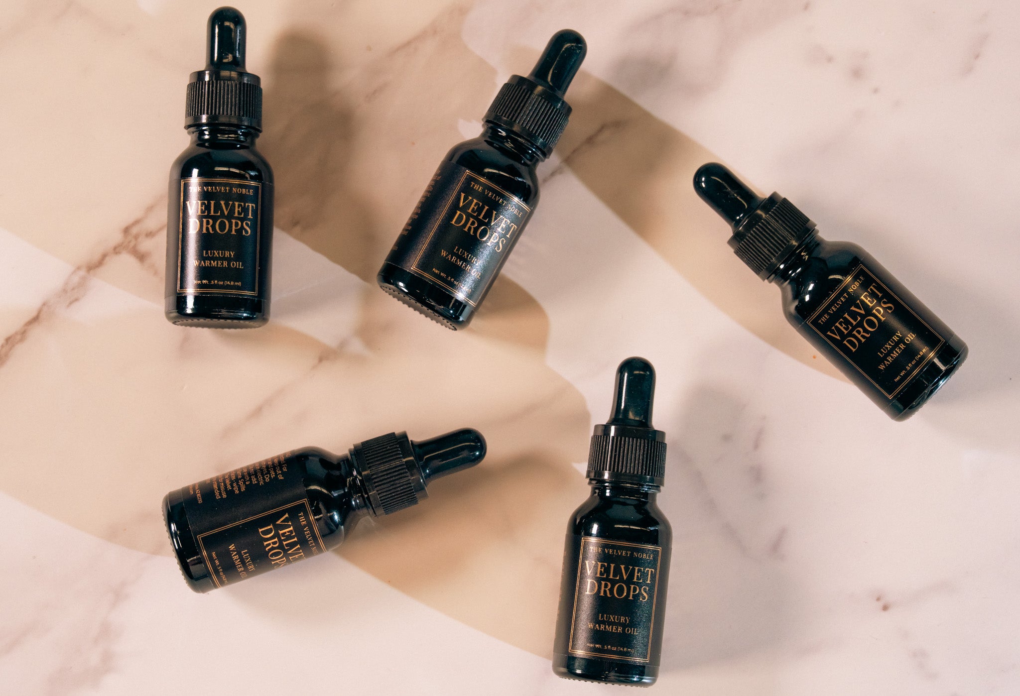 Five black bottles labeled 'Velvet Drops' on a marble surface