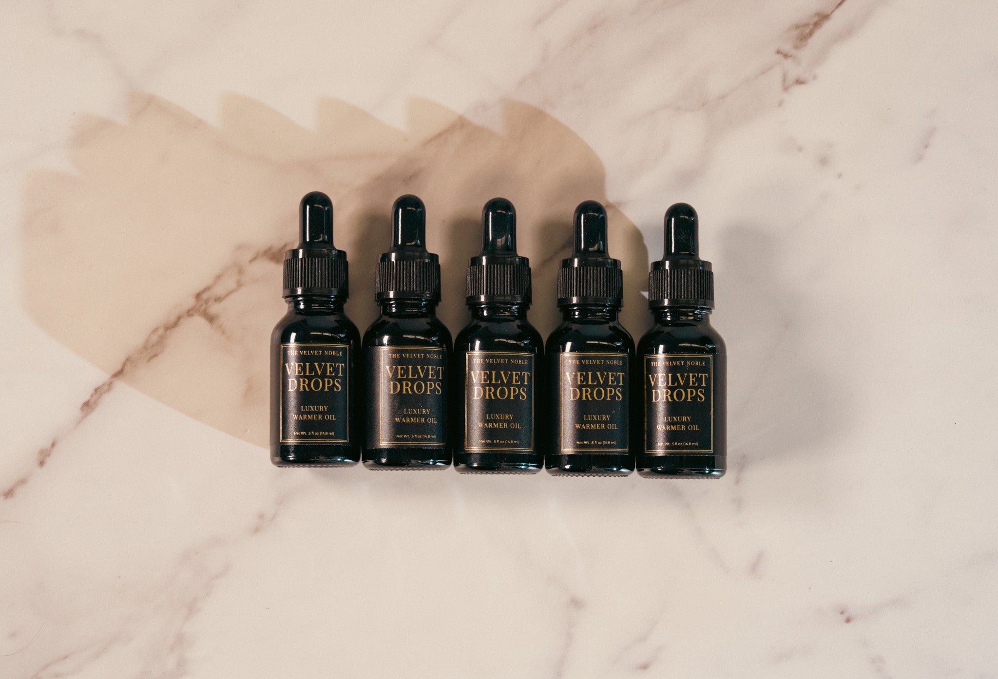 Five black bottles labeled 'Velvet Drops' on a marble surface