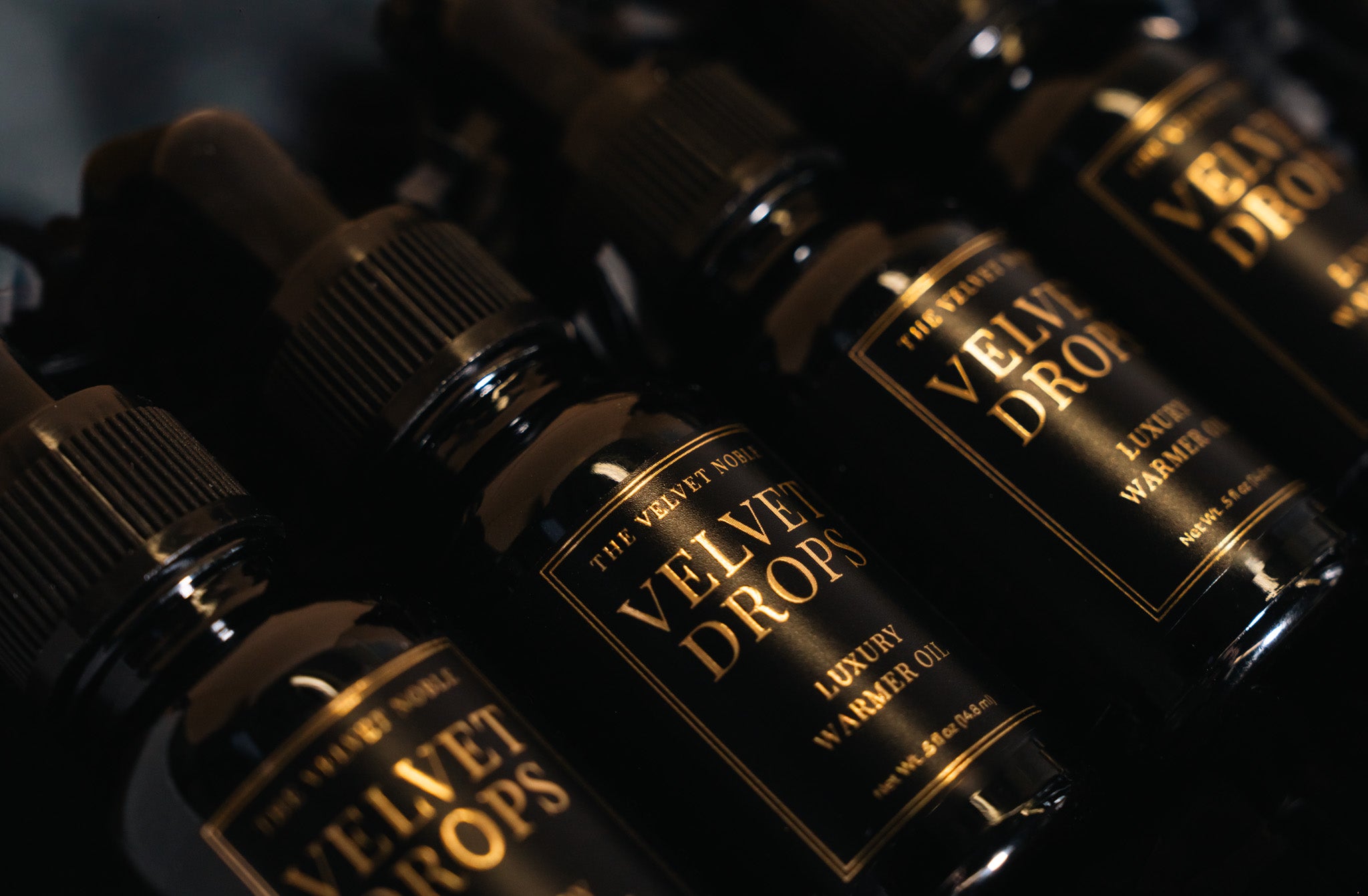 Bottles of 'Velvet Drops' luxury warmer oil on a dark background