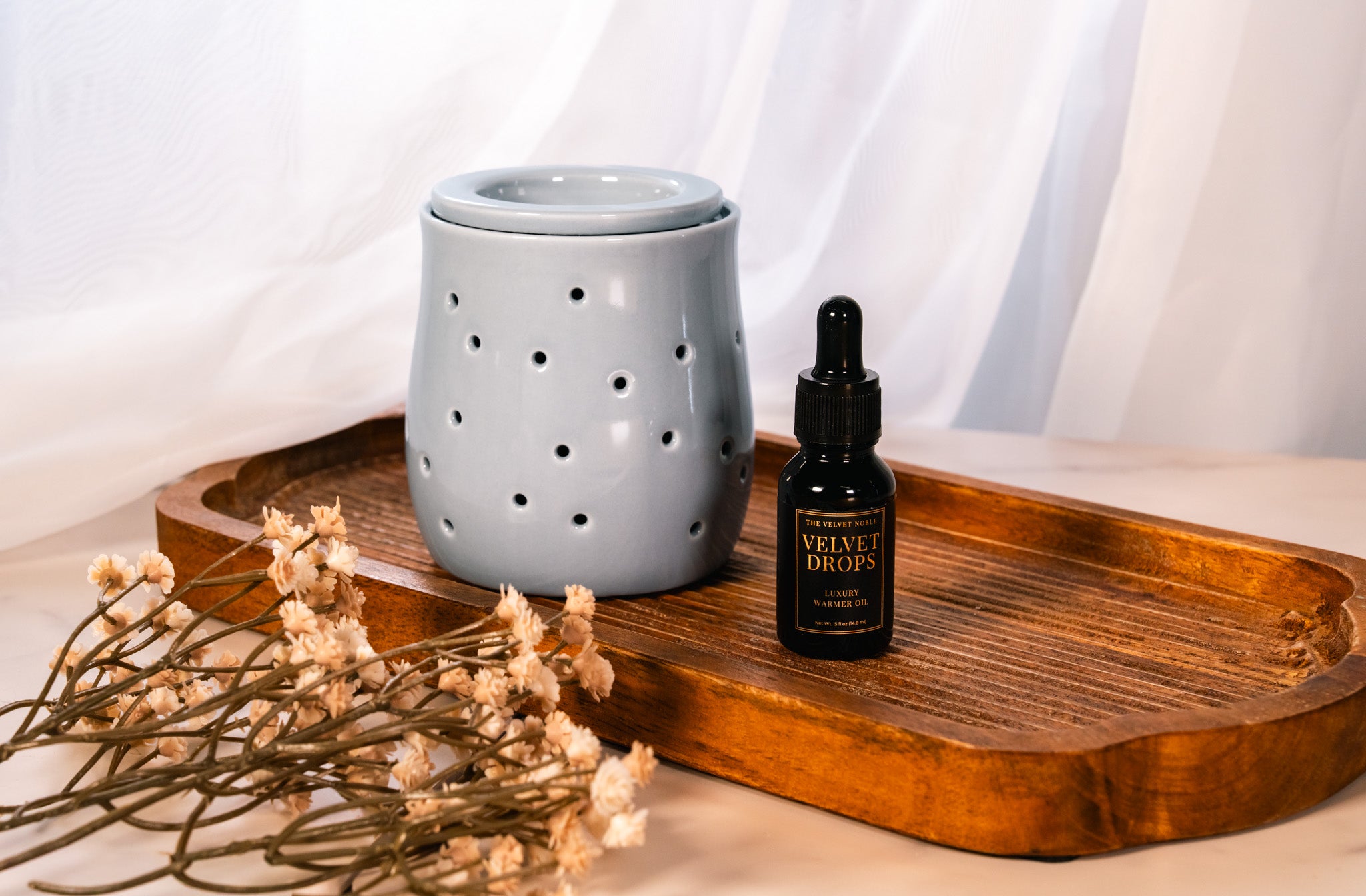 Petite fragrance warmer with a discovery set sized Velvet Drops on a wooden tray with floral elements.