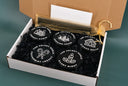 5 black candle tins labeled, each labeled differently on the lid with 5 lids" The Velvet Noble, Forest Cabin, Evening Snow, Ginger Bells, Peppermint Legacy and Silent Night." All 5 tins are placed into a white and brown cardboard box filled with tiny black paper packing confetti. Tucked into the box is also a white envelope and a gold bag with a black wand tray and a 2 stirring wands for the candles. 