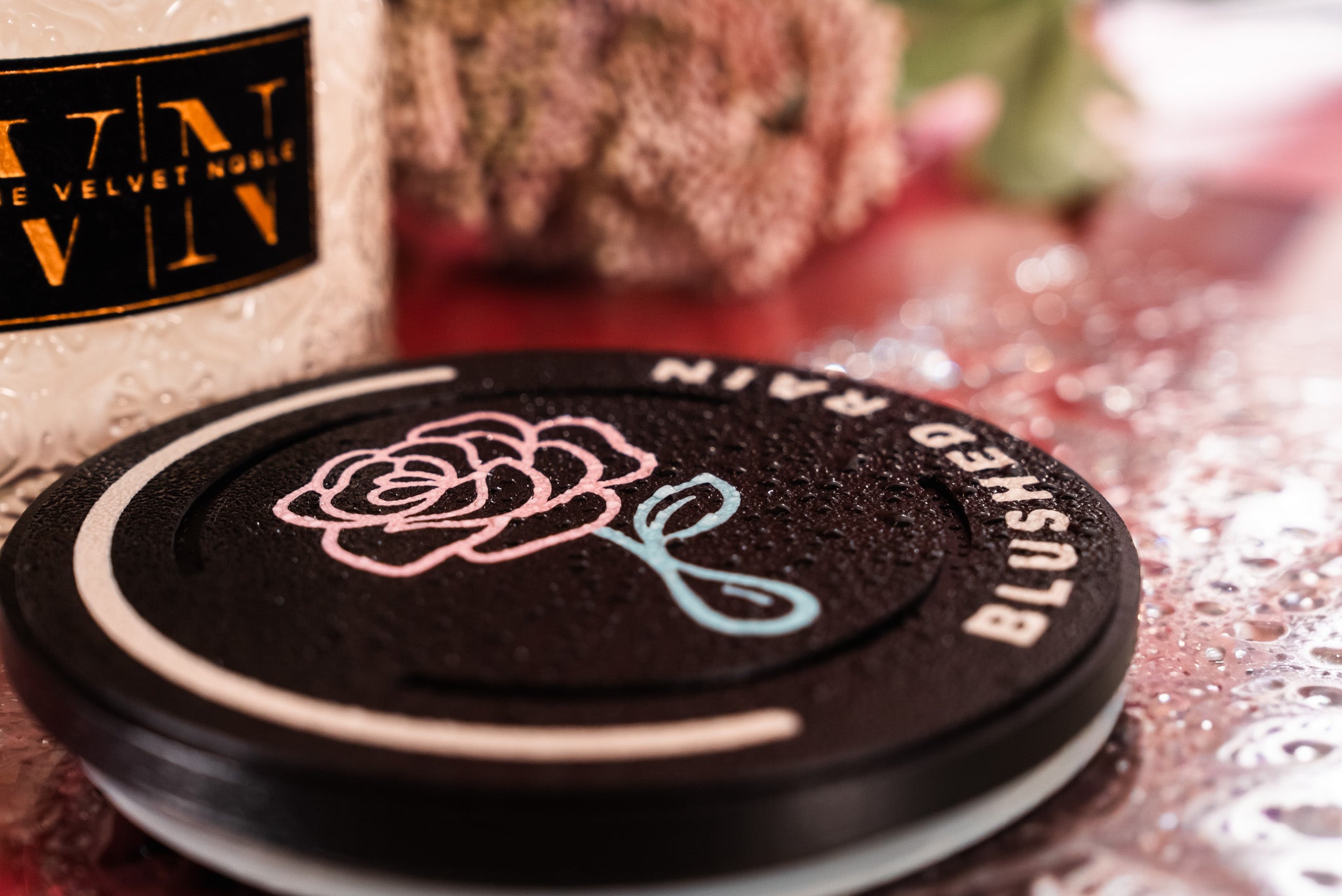 Blushed Rain Lid with water droplets on it on a pink surface.