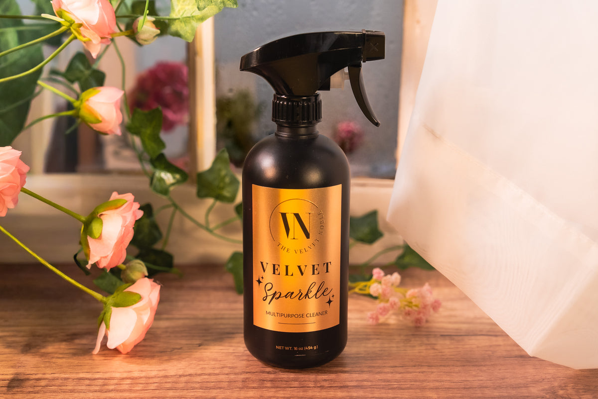 Spray bottle labeled 'Velvet Sparkle' on a wooden surface with flowers in the background