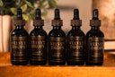 Five bottles of Velvet Drops luxury warmer oil on a wooden surface with a blurred background.