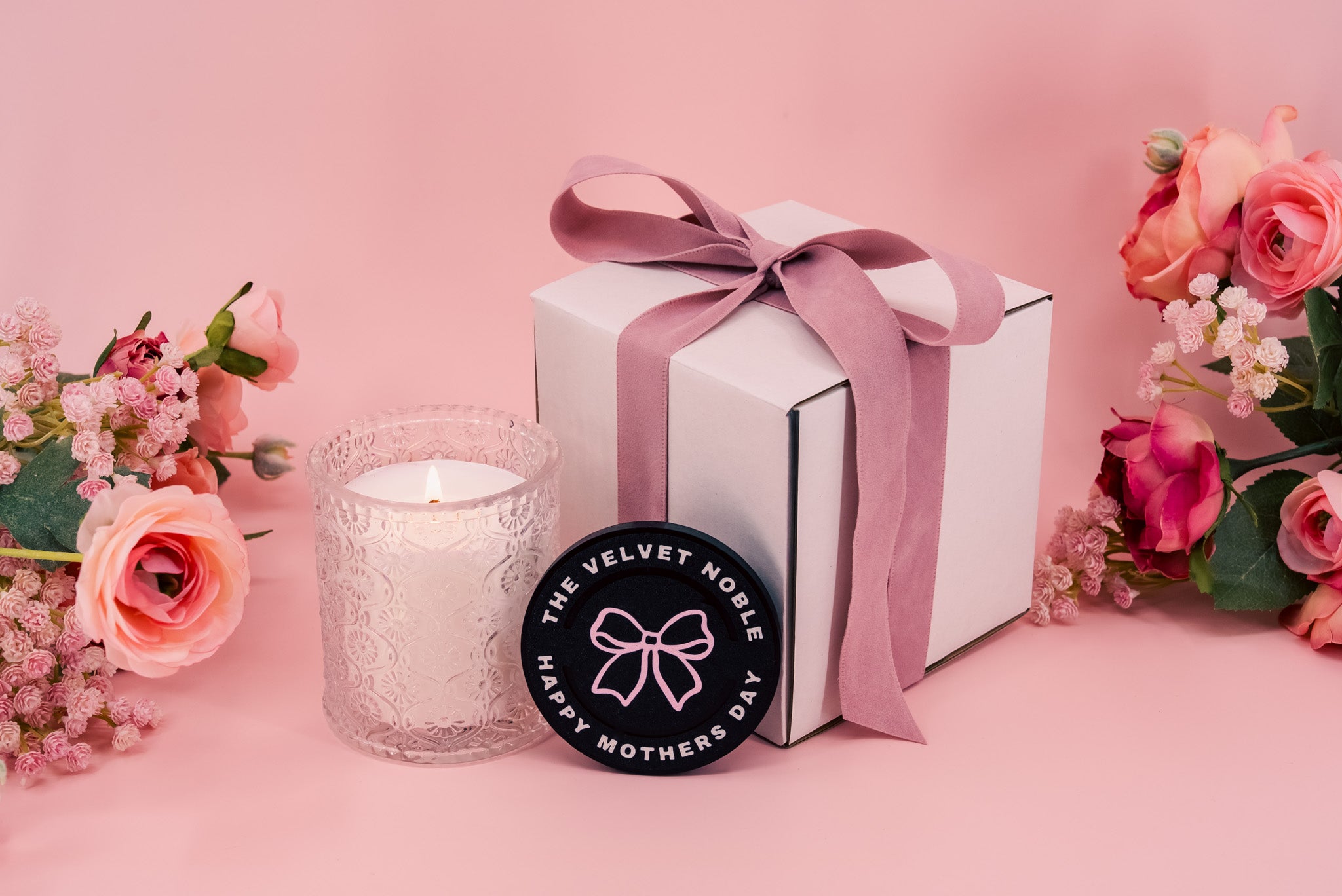 Candle, gift box with pink ribbon, and Mother's Day Velvet Noble candle lid on a pink background