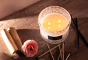 2-wick candle on a wooden surface with a flower, vanilla and some matches.