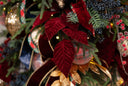 Close-up of a deep red velvet leaf, green pine branches, gold ribbons, plaid accents, and small warm string lights.