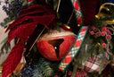 A large red and gold chorusline bell, on a decorated green Christmas tree with red velvet leaf stems, plaid ribbon and red berries. 