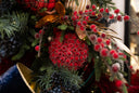 A close-up of a red berry ball ornament with small black dots on the smaller balls on the berry ornament, on a green tree with other blue and red accents. 