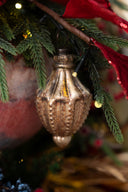 A vintage-style metallic gold Christmas ornament hanging from a decorated Christmas tree branch with green pine needles and red ribbon.