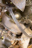 Close-up of a metallic silver ribbon with glittery gold ornaments, a glossy gold bauble, and soft cream ribbons.