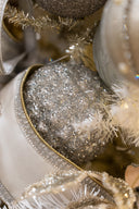 Close-up of a silver glitter Christmas ornament nestled among white ribbons, gold trim, and tinsel on a decorated tree.