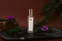 Black Vintage Mini Air & Linen Mist with gold cap and white label on a dark surface with purple flowers and greenery.