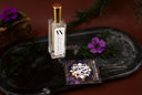 Black Vintage Mini Air & Linen Mist with gold cap and white label on a dark surface with purple flowers and greenery.
