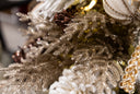 Gold metallic, glittering pine bush decor spray, nestled into a white and gold decorated Christmas tree.