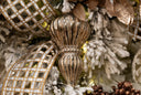 A close-up of a metallic gold Christmas tree ornament with a ribbed, textured finish, nestled among white frosted faux snow branches, glittery gold leaves, and a gold-and-white checkered ribbon.