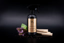 A black spray bottle labeled 'Velvet Sparkle' with a gold label, styled with vanilla beans, purple flowers, and coffee beans on a dark background.