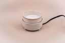 A ceramic fragrance warmer with a textured cream-colored base and a white inner cup, featuring a black power cord on a solid beige background.