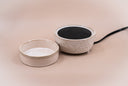 A ceramic fragrance warmer, featuring a textured cream-colored exterior and a black interior heating element, shown on a solid beige background.
