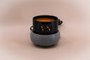 A black wax warmer candle with a textured gray fragrance warmer, featuring a gold logo that reads 'VN The Velvet Noble'. The candle is filled with amber-colored wax and sits on a neutral beige background.