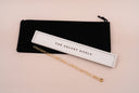 A clear and gold specked wand with a white and gold tray with 'THE VELVET NOBLE'  printed in it and a black velvet drawstring pouch, all on a light tan background.
