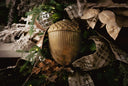 A large ribbed metallic gold acorn ornament nestled among green pine branches, glittery gold leaves, and patterned ribbon on a dark holiday tree.