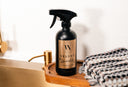 Spray bottle labeled 'Velvet Sparkle' on a wooden tray with a bath tub and towel in the background.