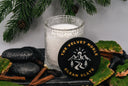 Candle with 'The Velvet Noble' logo on a decorative setting with stones and foliage.