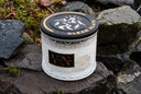 White candle with black lid featuring branding on a stone surface