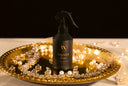 Black spray bottle labeled 'Velvet Home' on a decorative gold tray with pearls and lights.