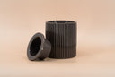 A dark brown ribbed warmer with its matching cup leaning against it, set against a solid beige background.