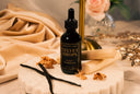 Bottle of 'Velvet Drops' on a marble surface with vanilla beans.