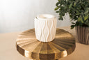 A textured, white fragrance warmer on a gold pedestal with a plant in the background