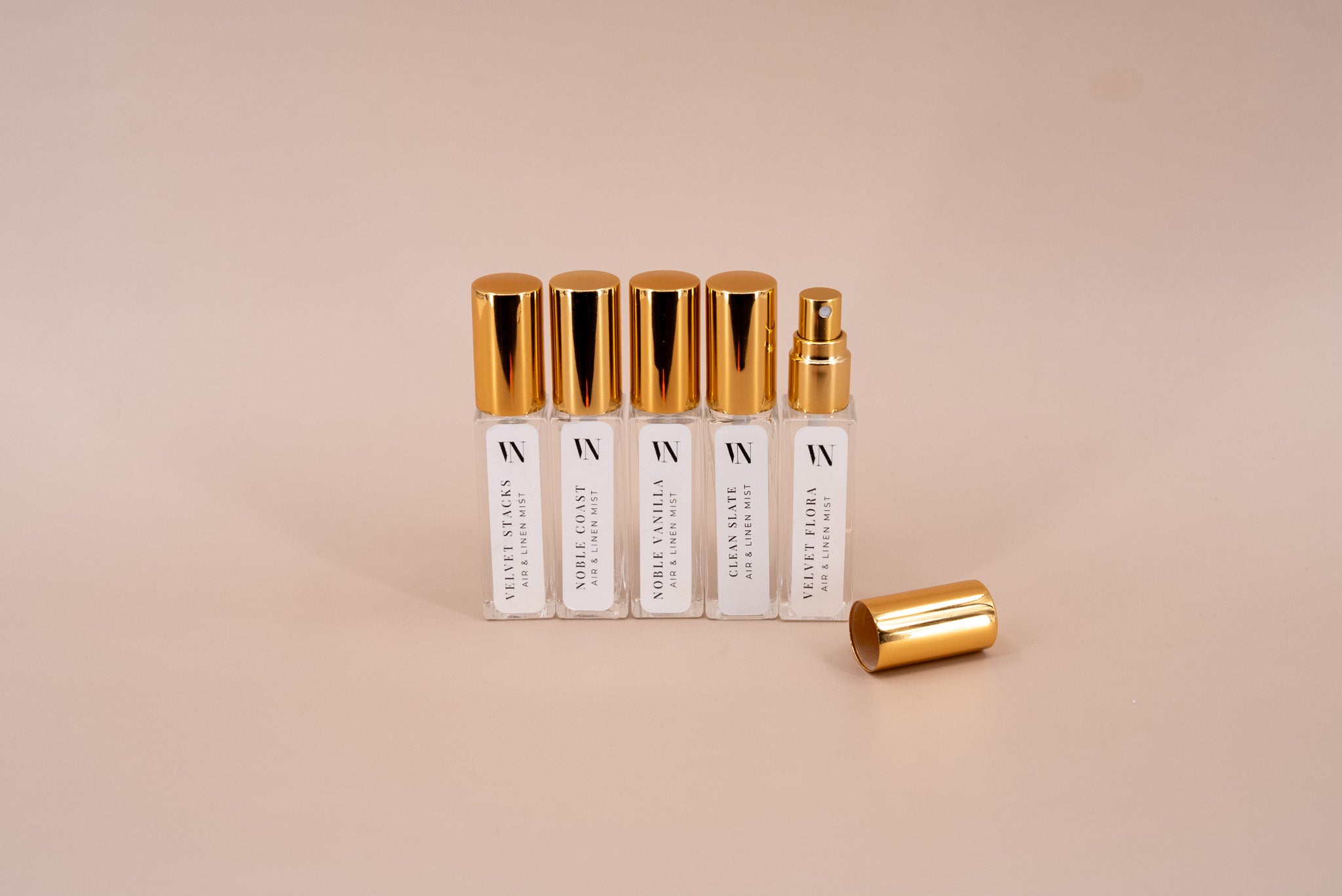 5 Small Air & Linen Mist bottles with golden caps. Velvet Stacks, Noble Coast, Noble Vanilla, Velvet Flora, & Clean Slate on a beige background.