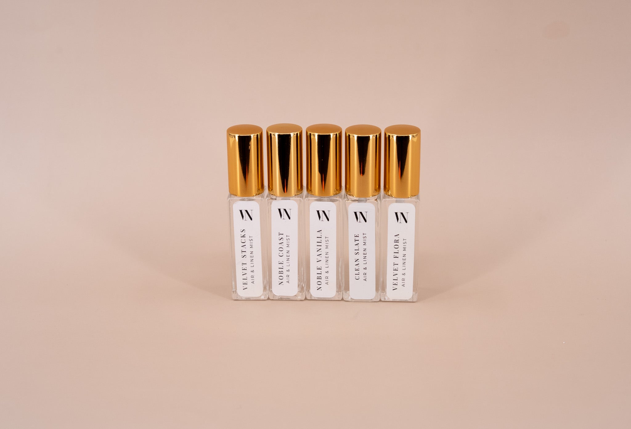 5 Small Air & Linen Mist bottles with golden caps. Velvet Stacks, Noble Coast, Noble Vanilla, Velvet Flora, & Clean Slate on a beige background.