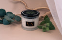 Velvet Ease candle with Driftwood, Eucalyptus leaves and other greenery on a beige background.
