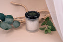 Velvet Ease candle with Driftwood, Eucalyptus leaves and other greenery on a beige background.