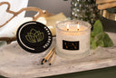 A lit Velvet Ease 2-wick candle on a marble surface with mint leaves and matches.